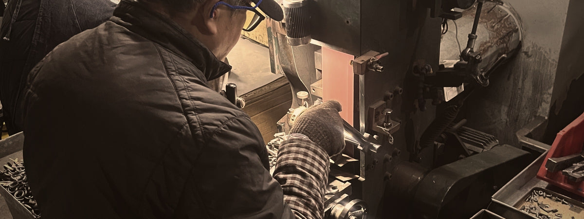 Operator hand-grinding a shear blade at a workbench under the machine work light
